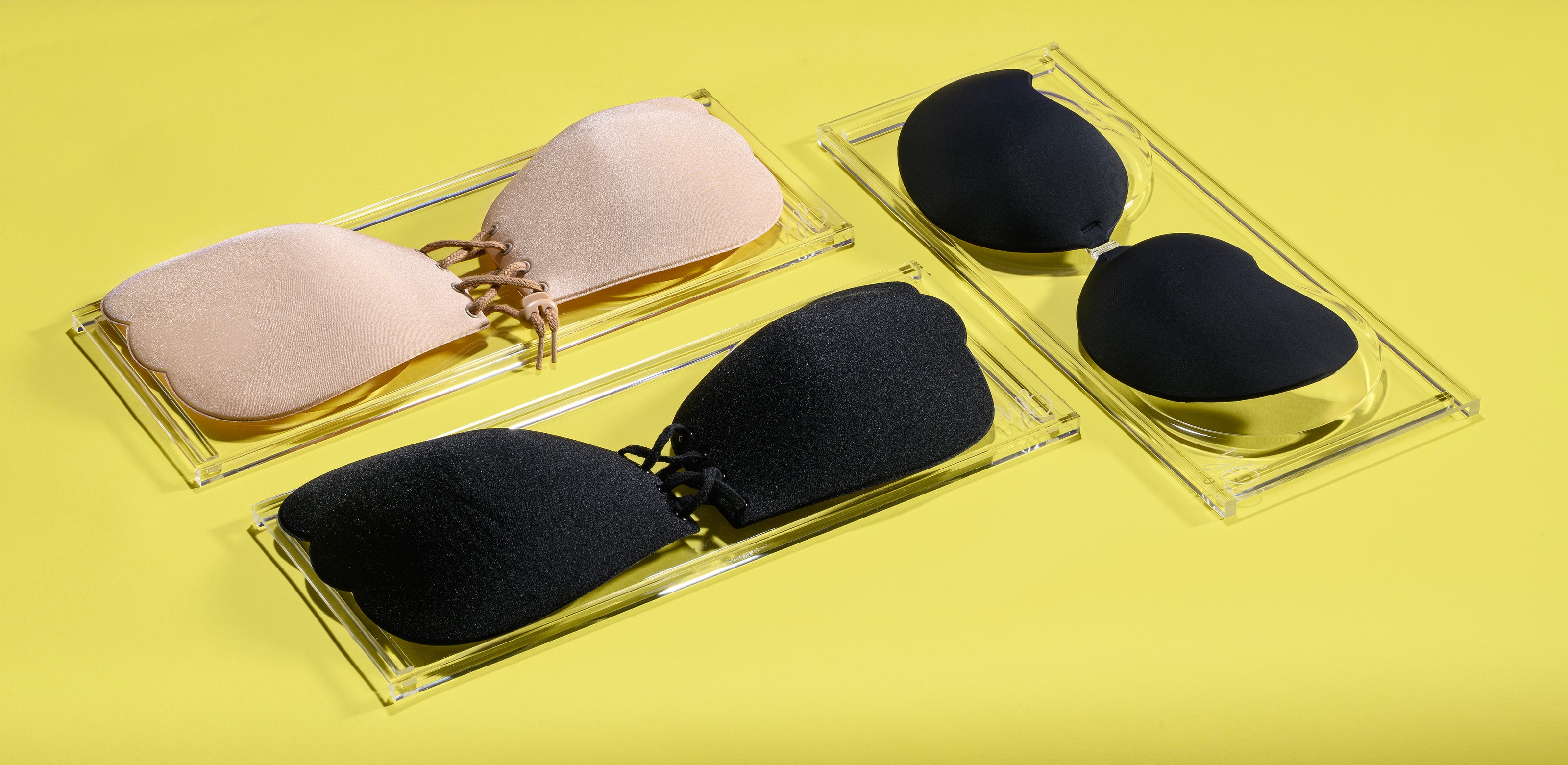 Two sets of black and pink silicone pads bra on clear stands against a yellow background