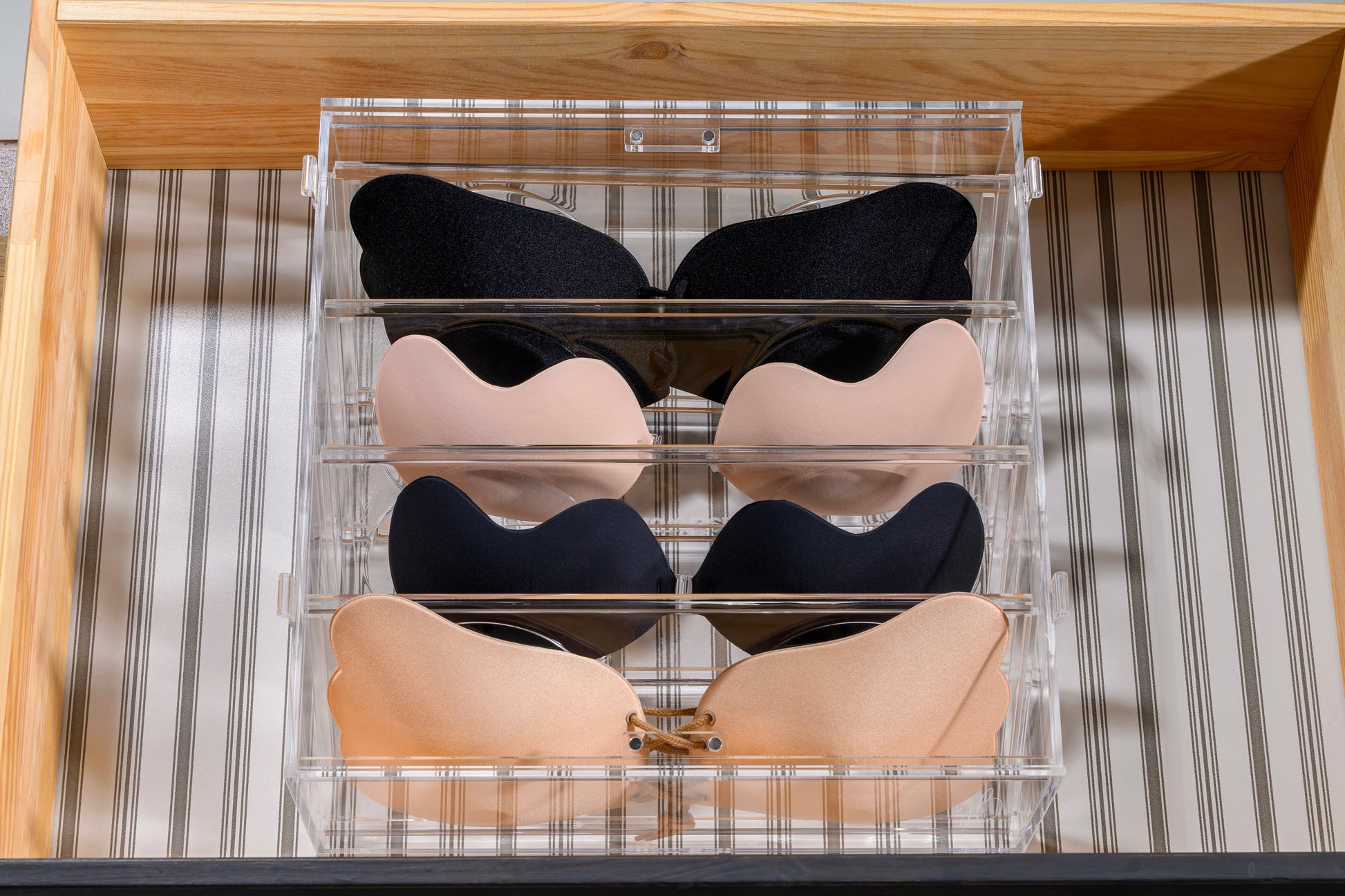 Set of black, beige, and navy bras in a clear organizer on a striped background