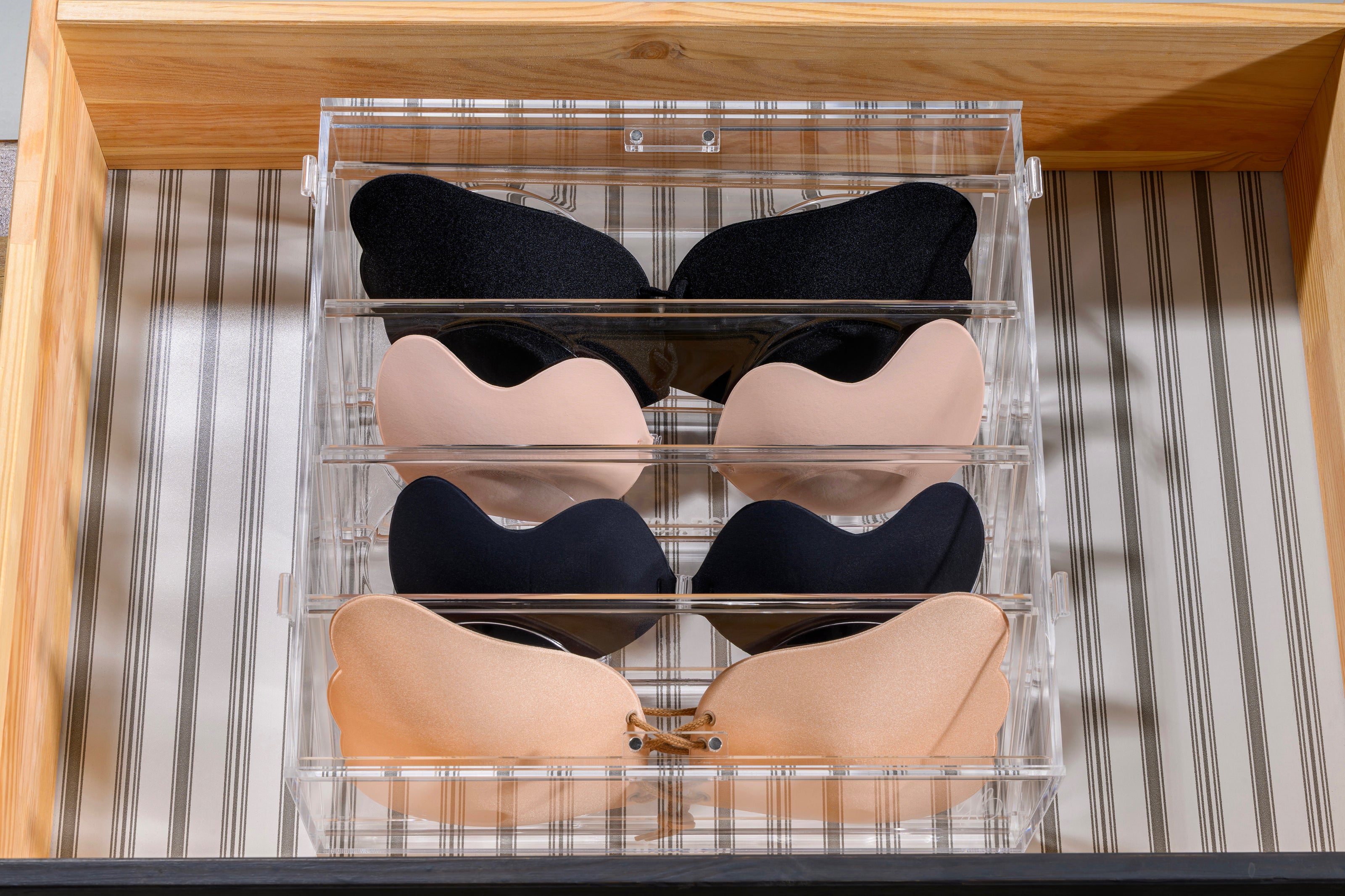 Set of black, beige, and navy bras in a clear organizer on a striped background